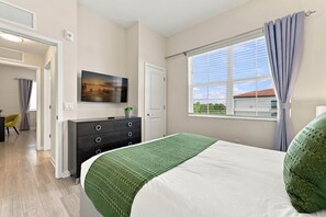 Ein Schlafzimmer mit Bett, Kommode, Fernseher und einem Fenster mit Vorhängen.