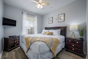 A bedroom with a bed, bedside tables, a TV, a ceiling fan, and a window with blinds. - Vista Cay 3BR Condo Pools Near Universal (Orlando)