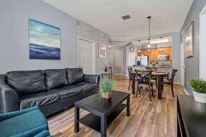 A modern living room with a black leather sofa, a coffee table, and a dining area with wooden chairs and a table. - Vista Cay 3BR Condo Pools Near Universal (Orlando)