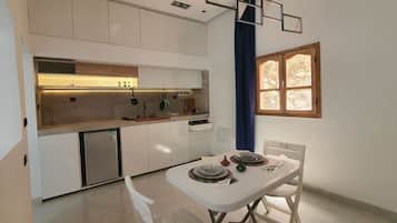 Una cucina compatta con elettrodomestici integrati, una zona pranzo con un tavolo apparecchiato per due e una finestra con vetri decorativi.