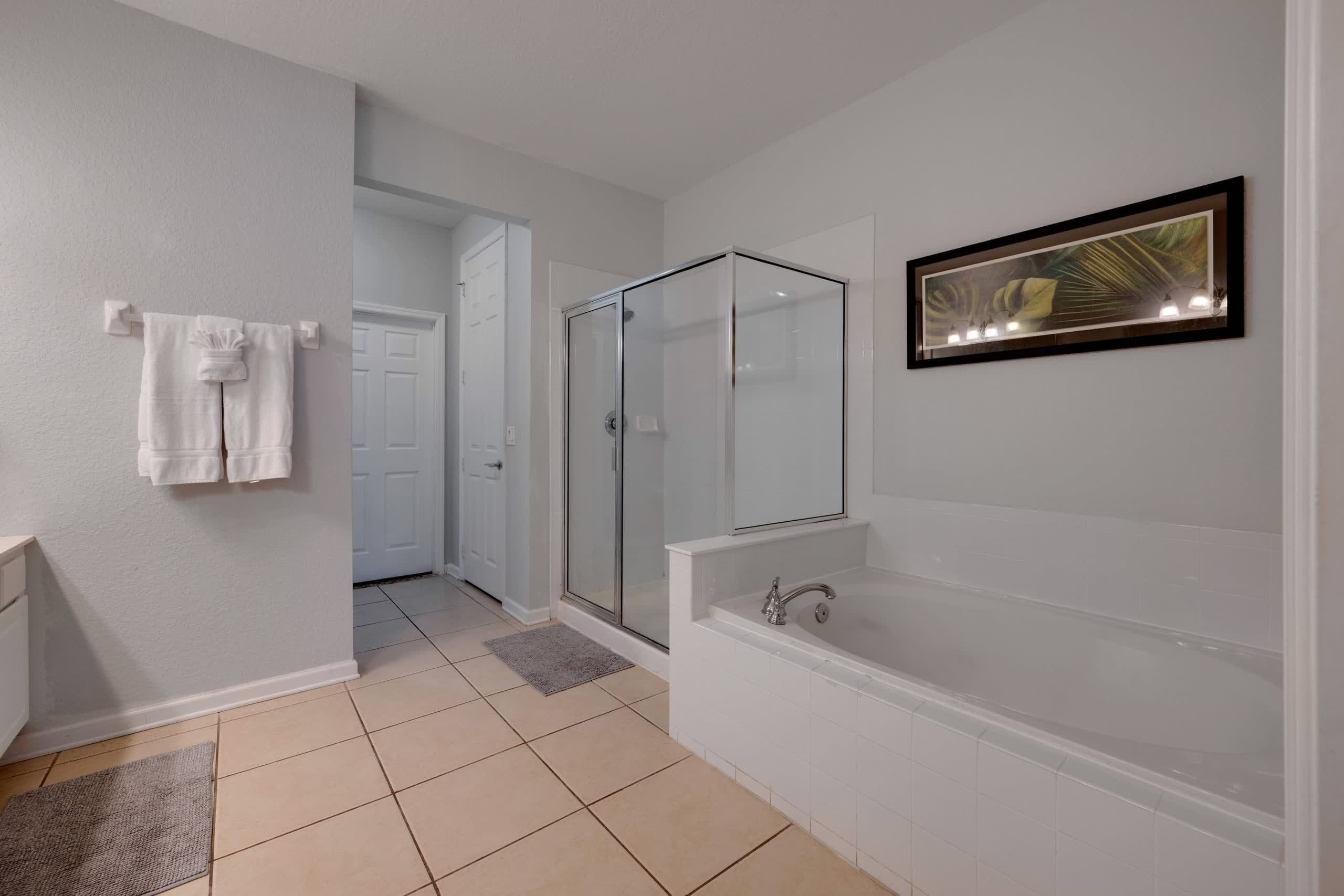 A modern bathroom with a glass-enclosed shower, a large bathtub, and a framed artwork on the wall.