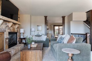 A living room with a stone fireplace, a sofa set, a coffee table, and a staircase. - Walk to Frostwood Gondola, private hot tub (Park City)