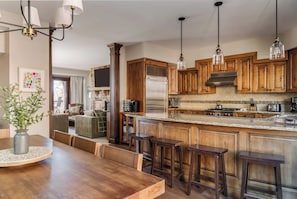 Tilava keittiö, jossa on puiset kaapit, suuri keittiösaareke jakkaroineen ja riippuvalaisimet.