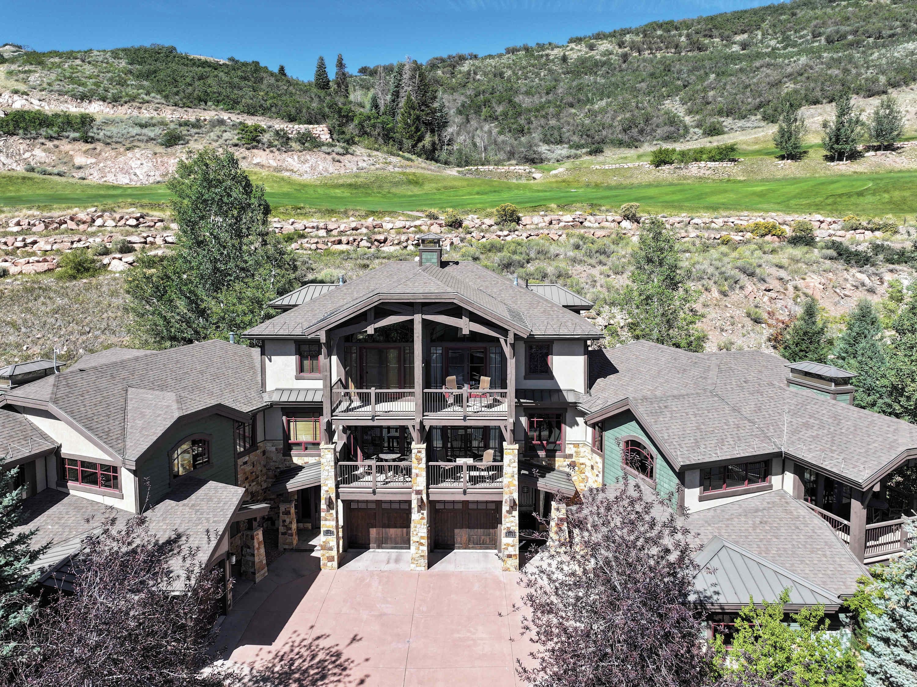 A large, multi-story building with a central balcony and multiple entry points, surrounded by a natural landscape.