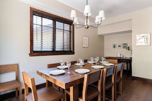 A dining area with a wooden table set for six, six chairs, a chandelier, and a large window with blinds. - Walk to Frostwood Gondola, private hot tub (Park City)