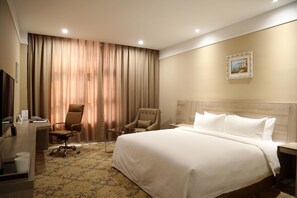 Une chambre d’hôtel avec un grand lit, un bureau avec une chaise, une télévision et une fenêtre avec des rideaux.