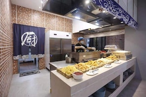 Un buffet proposant une variété de plats, un espace cuisine avec un chef, et un mur en briques.