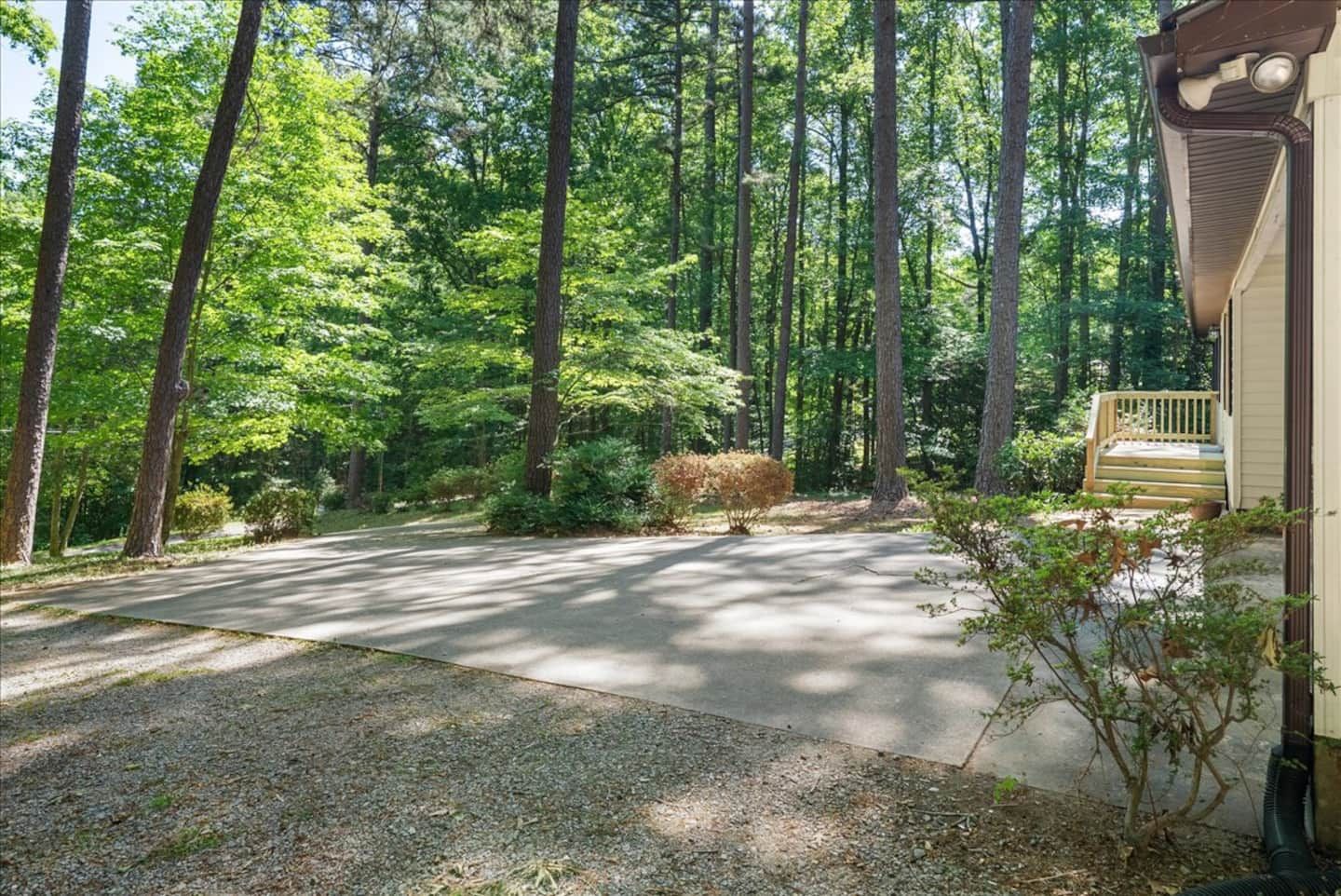 A residential driveway leading to a house with a porch, surrounded by a forested area.