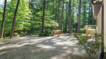 A residential driveway leading to a house with a porch, surrounded by a forested area.