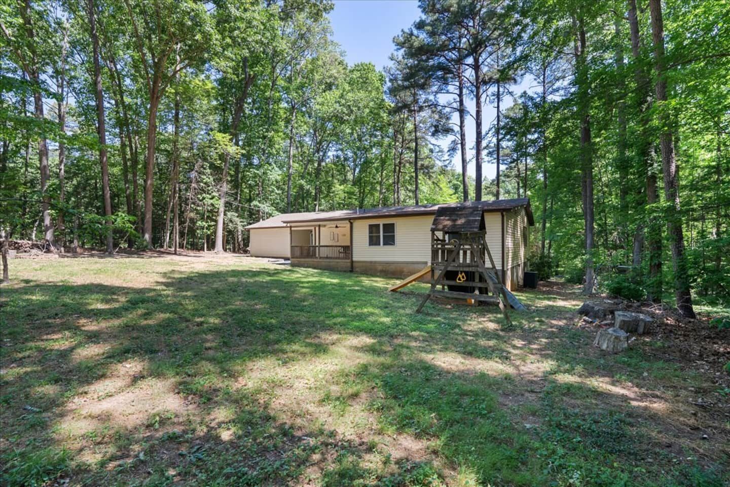 A single-story cabin with a fenced yard, surrounded by tall trees.