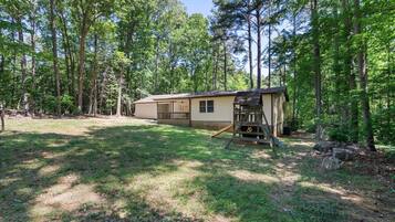 A single-story cabin with a fenced yard, surrounded by tall trees.