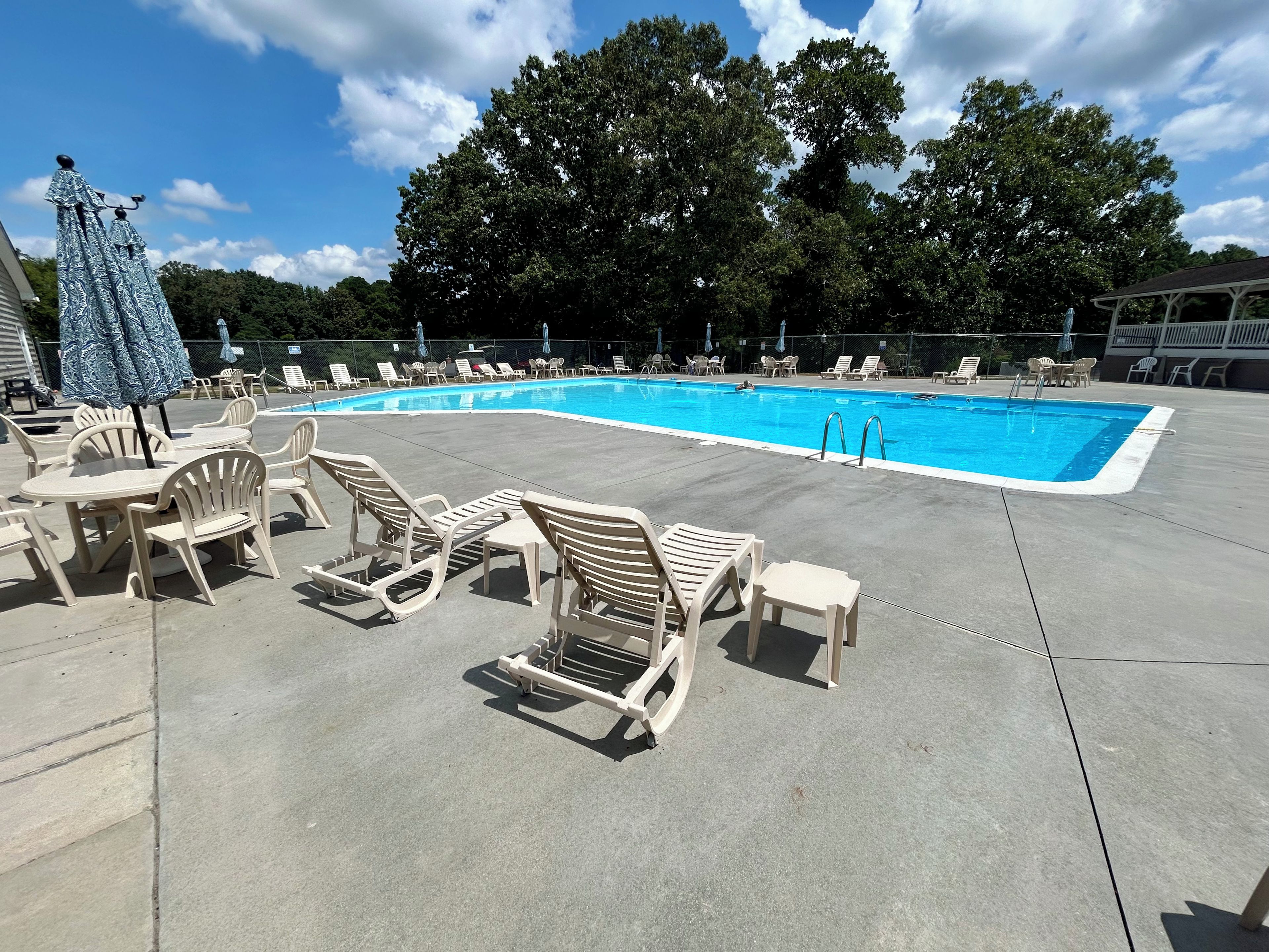 A swimming pool with lounge chairs and umbrellas, surrounded by trees and a clear sky.