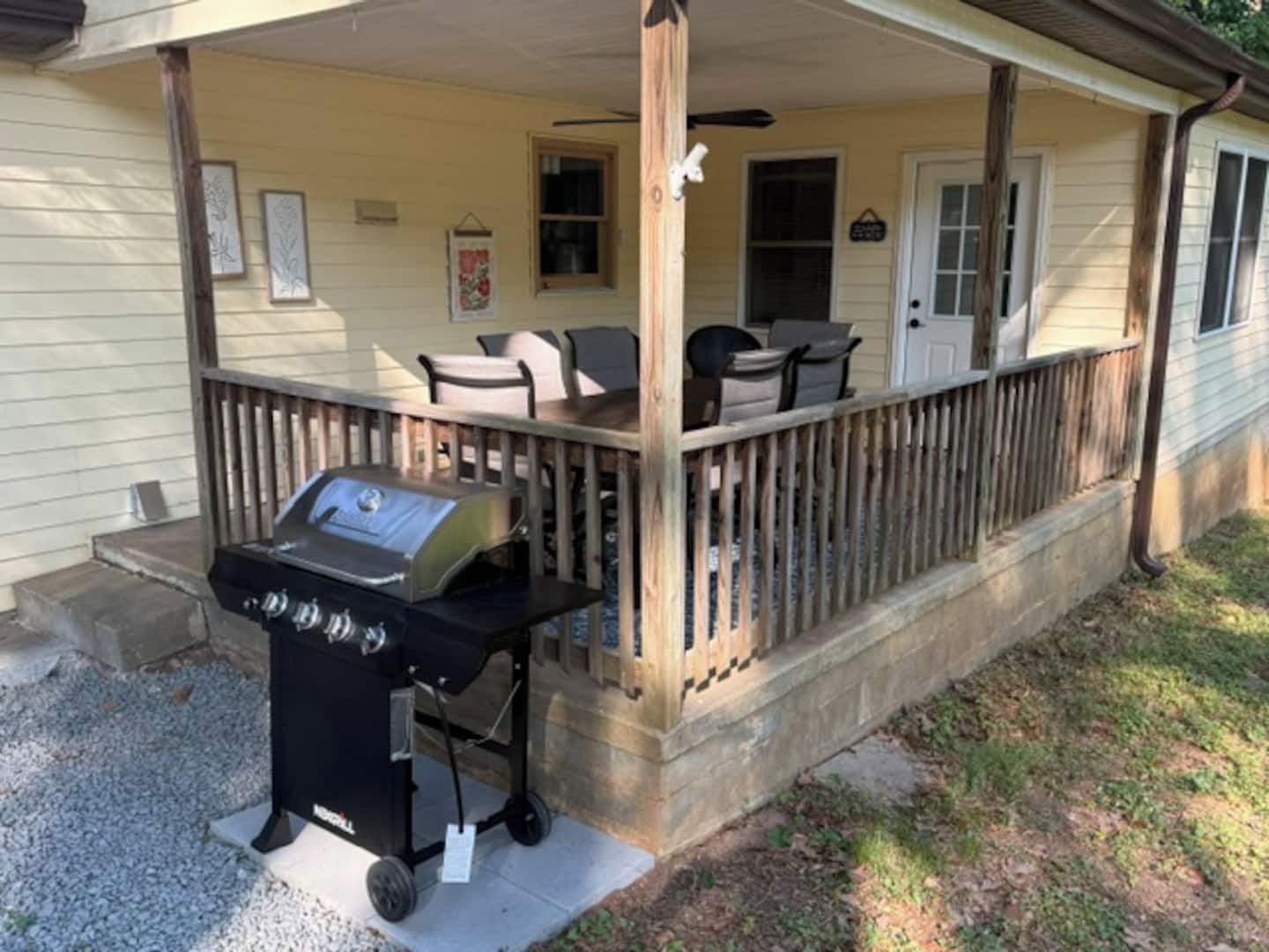 A covered porch with a grill, outdoor seating, and a wooden railing.