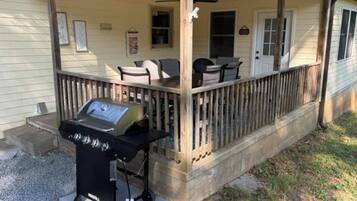 A covered porch with a grill, outdoor seating, and a wooden railing.