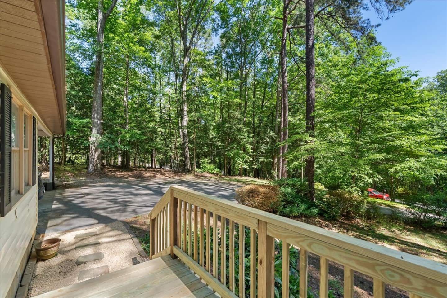 A wooden deck leading to a covered porch with a view of a forested area.