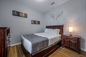 A bedroom with a wooden bed, a nightstand, a dresser, and two wall art pieces. - Vista Cay 3BR Condo King Suite Near Universal (Orlando)