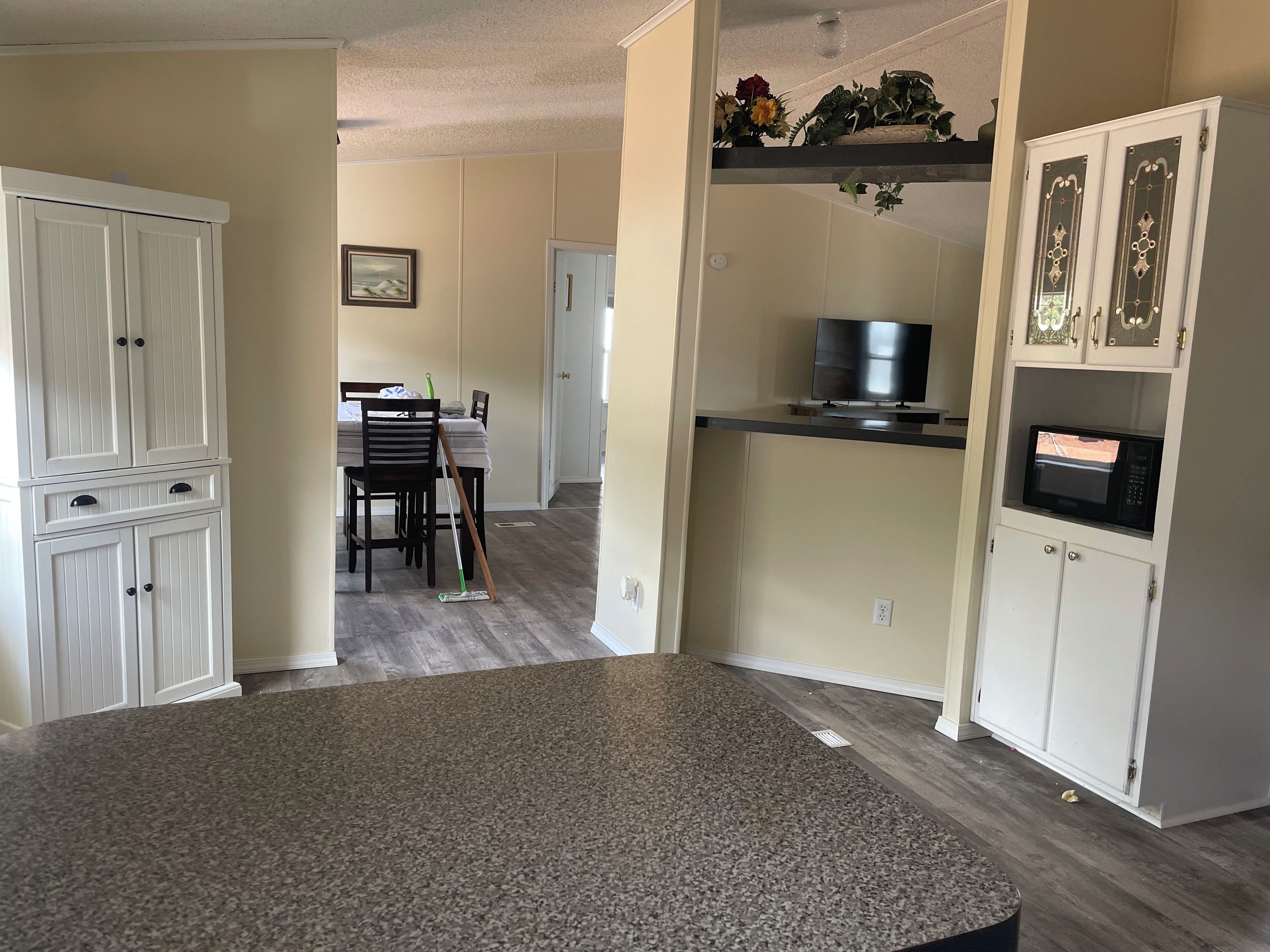 A kitchen with a granite countertop, white cabinetry, a microwave, and a dining area with chairs and a table.