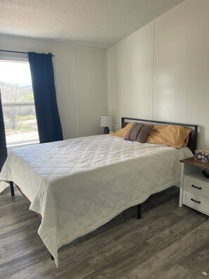 A bedroom with a bed, bedside table, lamp, and a window with curtains. - Mountain home located below Carlito Springs trail and convenient to Albuquerque. (Cedar Crest)