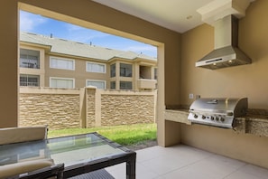An outdoor patio with a glass table, a barbecue grill, and a view of a residential building. - 3 Suites Private Hot Tub Near Disney (Kissimmee)