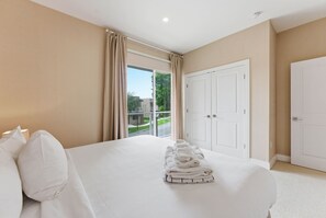 A hotel room with a large bed, a set of white towels, a sliding glass door to the outside, and a white door. - 3 Suites Near Disney Patio Grill & Balcony (Kissimmee)