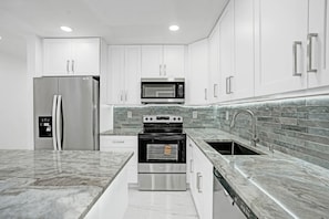 Una cocina moderna con armarios blancos, electrodomésticos de acero inoxidable, un salpicadero azulejado y una encimera de mármol.