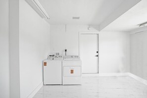 Una sala amb bugaderia, amb rentadora i assecadora, una porta i un sòl de rajola.
