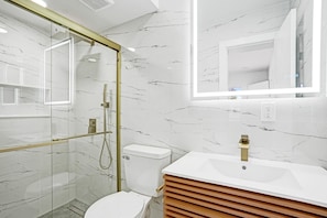 Un baño moderno con ducha envuelta en vidrio, inodoro blanco y tocador con grifo dorado.