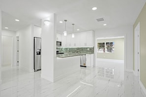 Una cocina moderna con armarios blancos, encimera de mármol e iluminación empotrada.