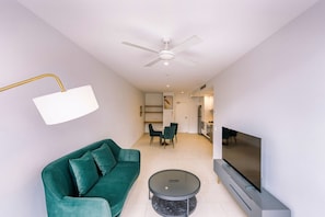 A modern living room with a green sofa, a round coffee table, a flat-screen TV, and a ceiling fan. - Chic 1 Bedroom Apartment in a Prime Location (Fortitude Valley)