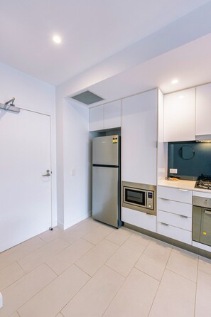 A modern kitchen with a built-in refrigerator, microwave, and gas stove. - Chic 1 Bedroom Apartment in a Prime Location (Fortitude Valley)