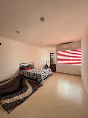 Ein Schlafzimmer mit einem Bett, einem Fahrrad, einem Fenster mit roten Jalousien und einer Decke mit Einbaustrahlern.