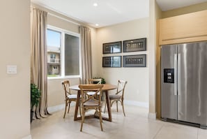 Eine moderne Küche mit einem Edelstahlkühlschrank, einem Esstisch mit vier Stühlen und einem großen Fenster mit Vorhängen.