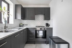 A modern kitchen with dark cabinets, a stainless steel sink, a gas stove, and a built-in oven. - Charming Parkside Apartment | WiFi | Gated Parking (Greater London)