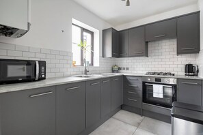 Een moderne keuken met grijze kastjes, een ingebouwde magnetron, een gasfornuis en een roestvrijstalen oven.