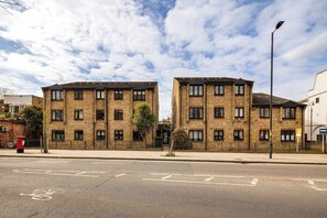 A two-story residential building with a brick facade, multiple windows, and a visible street in front. - Charming Parkside Apartment | WiFi | Gated Parking (Greater London)