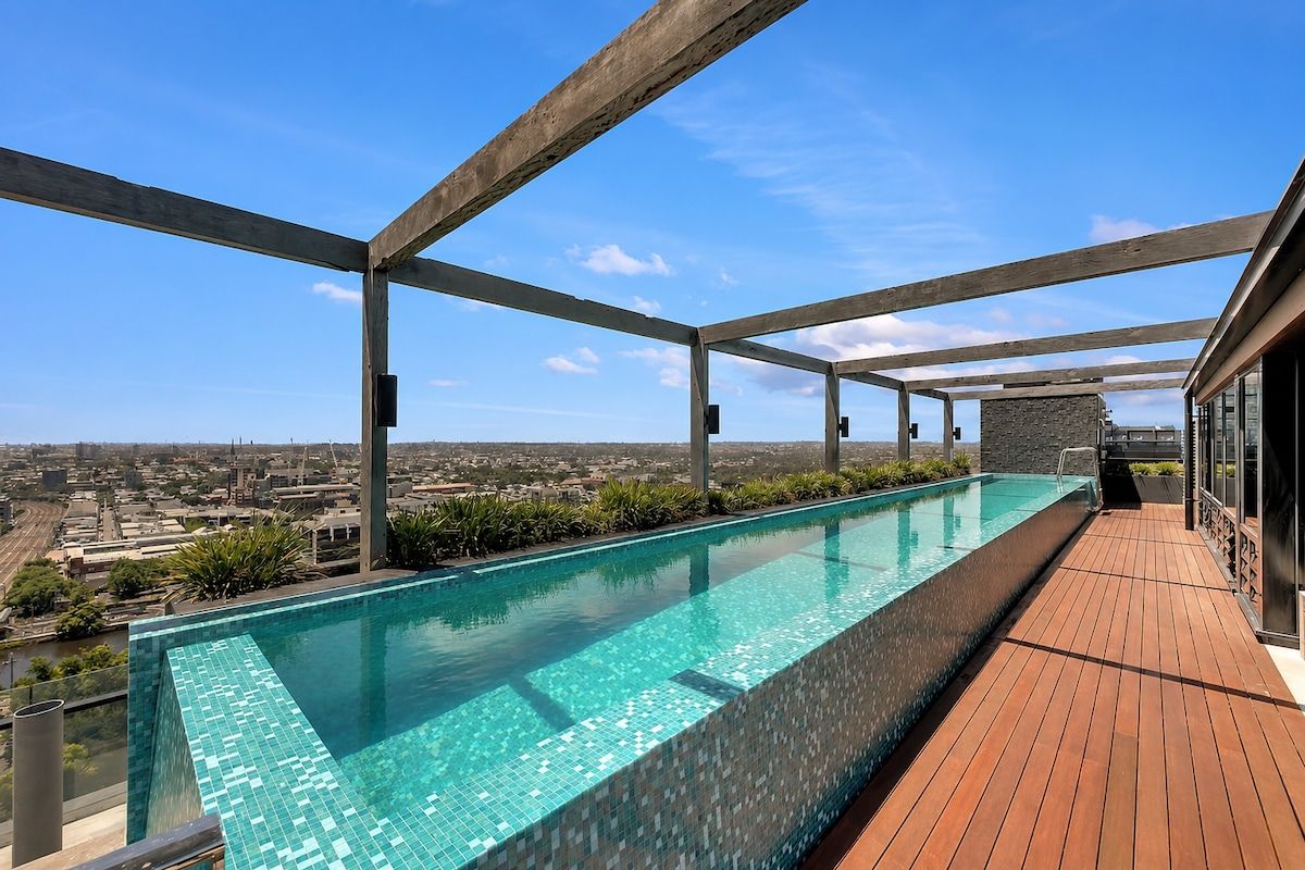 A rooftop infinity pool with a city view, wooden deck, and metal beams.