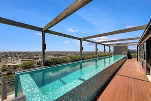 A rooftop infinity pool with a city view, wooden deck, and metal beams. - Panoramic City Views 3BR w Rooftop Pool & Parking (South Yarra)