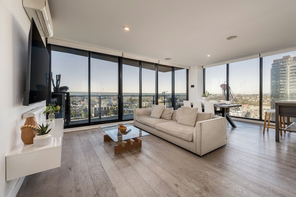 A modern living room with a large window, a sofa, a coffee table, and a flat-screen TV.