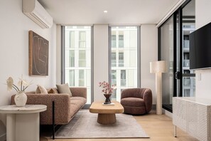 A modern living room with a sofa, armchair, coffee table, and a TV. - Resort-Style 2BR Living with Pool, Gym and Sauna (South Melbourne)
