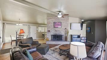 A living room with a fireplace, leather sofas, a coffee table, and a ceiling fan.