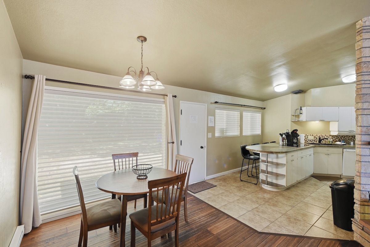 A compact kitchen with a dining area, a chandelier, and a view through the window blinds.
