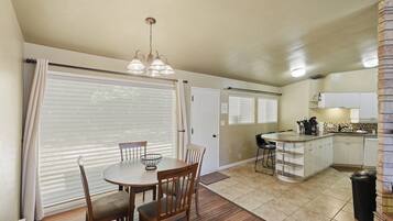 A compact kitchen with a dining area, a chandelier, and a view through the window blinds.