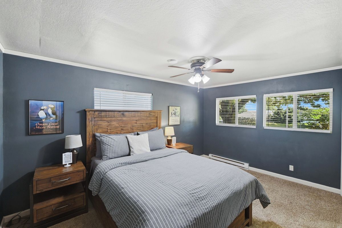 Une chambre à coucher avec un lit, des tables de chevet, un ventilateur de plafond et une fenêtre avec des stores.