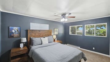 Une chambre à coucher avec un lit, des tables de chevet, un ventilateur de plafond et une fenêtre avec des stores.