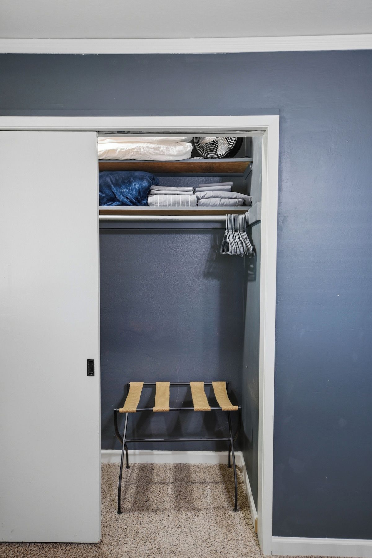 Un placard avec un banc, un ventilateur et des vêtements pliés.