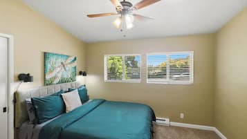 A bedroom with a bed, a ceiling fan, a window with blinds, and a wall-mounted artwork.