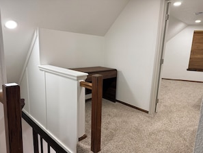 Ein Zimmer mit schrägen Wänden, einem Holztisch, einer weißen Wand und einem Teppichboden.