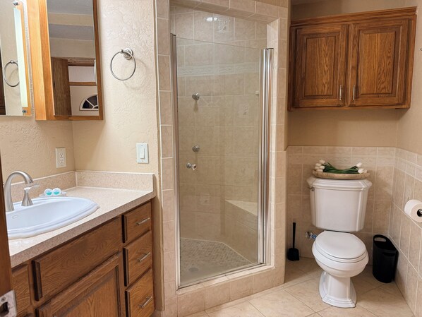 A bathroom with a shower, toilet, sink, wooden cabinets, and a mirror.