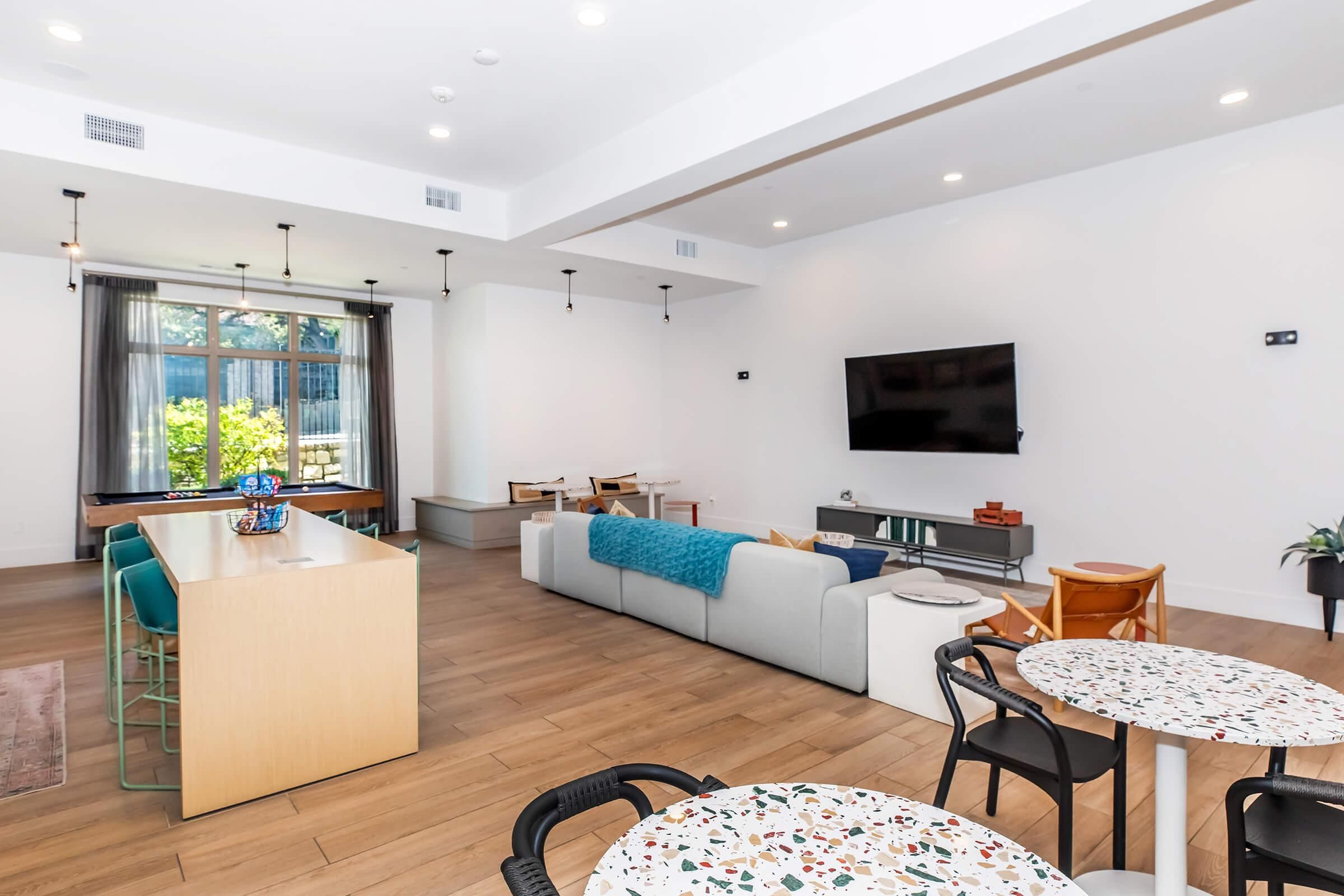 A modern living room with a pool table, a sofa, a coffee table, and a TV mounted on the wall.