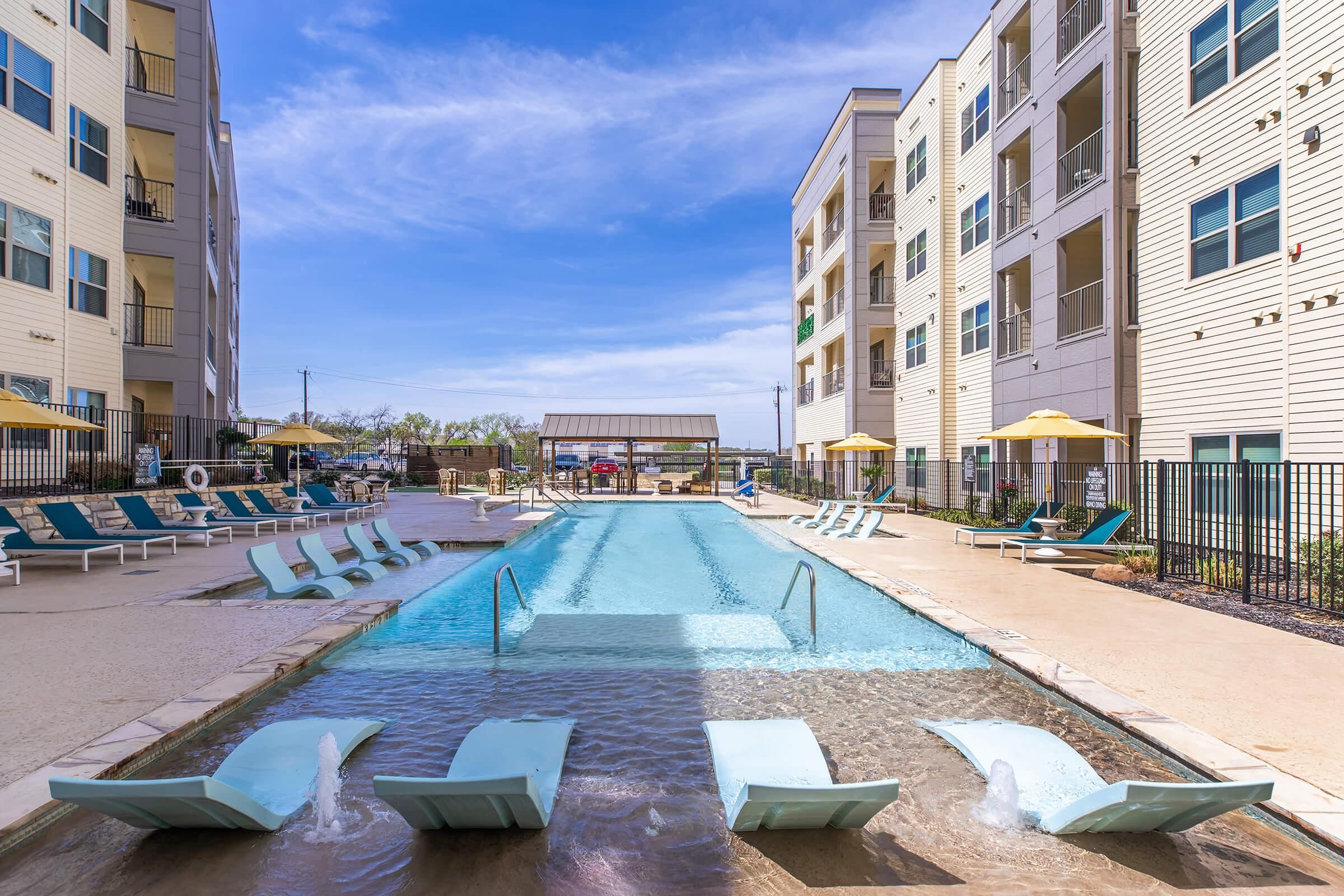 Ein Swimmingpool mit Liegestühlen und Sonnenschirmen, umgeben von Wohngebäuden.
